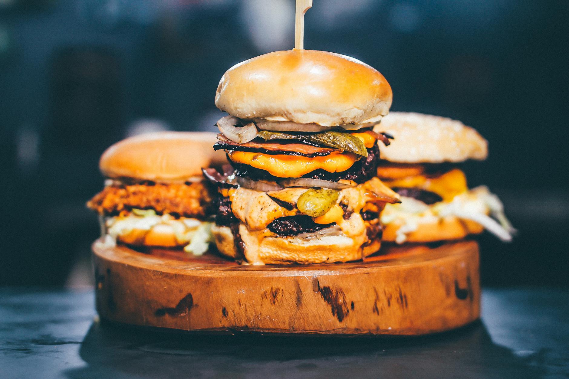 Close-up of a delicious cheeseburger trio with juicy beef, melted cheese, and fresh toppings on a wooden surface.